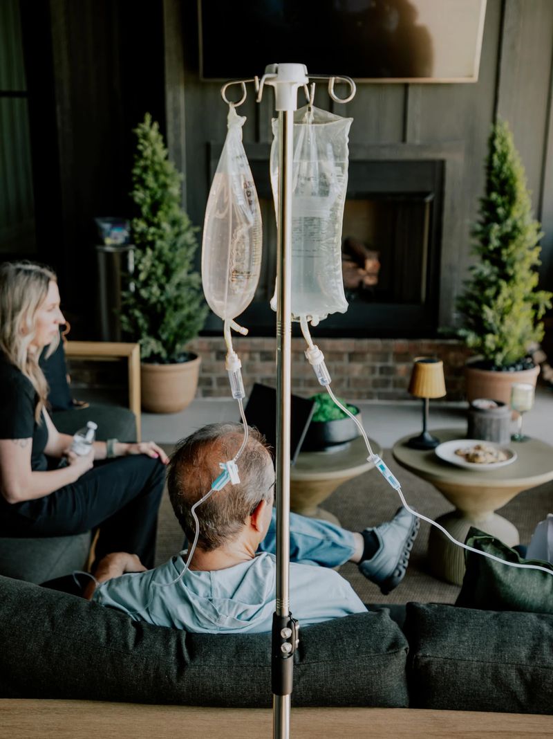Several people resting with IV drips in a living room while a nurse checks on them